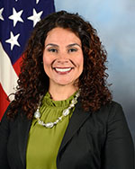 Ms. Kelly Cruz standing in front of a flag.